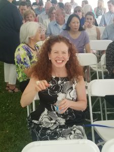 Mary Coons smiling at William Coons' high school graduation from Franklin Academy. She is wearing a black dress with white flowers on it.