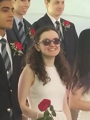 Kelly Coons in a white dress at her high school graduation, holding a red rose and smiling.