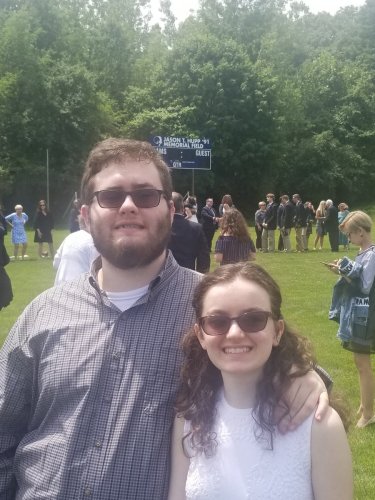 Kelly Coons in a white dress at her high school graduation with her twin brother, William Coons IV, in a gray button-down shirt.