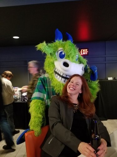 Mary Coons smiling with the Hartford Yard Goats mascot, a green goat with blue horns named Chompers.